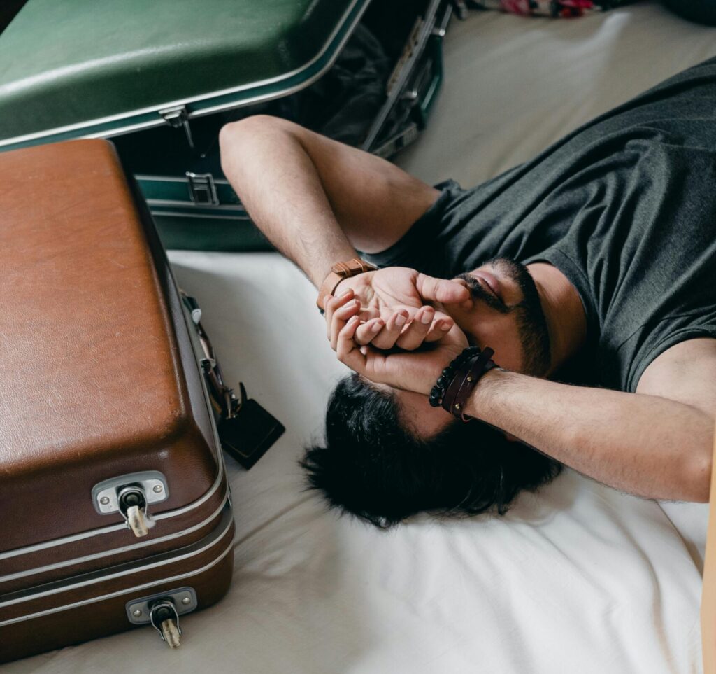 A young man rests on a bed, surrounded by luggage, reflecting a travel or moving theme.