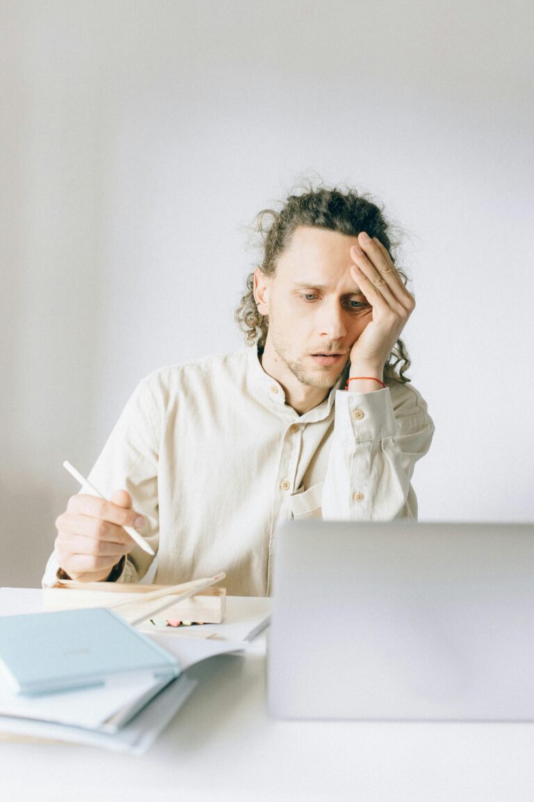 Young man overwhelmed by work at his desk, showing stress and fatigue.