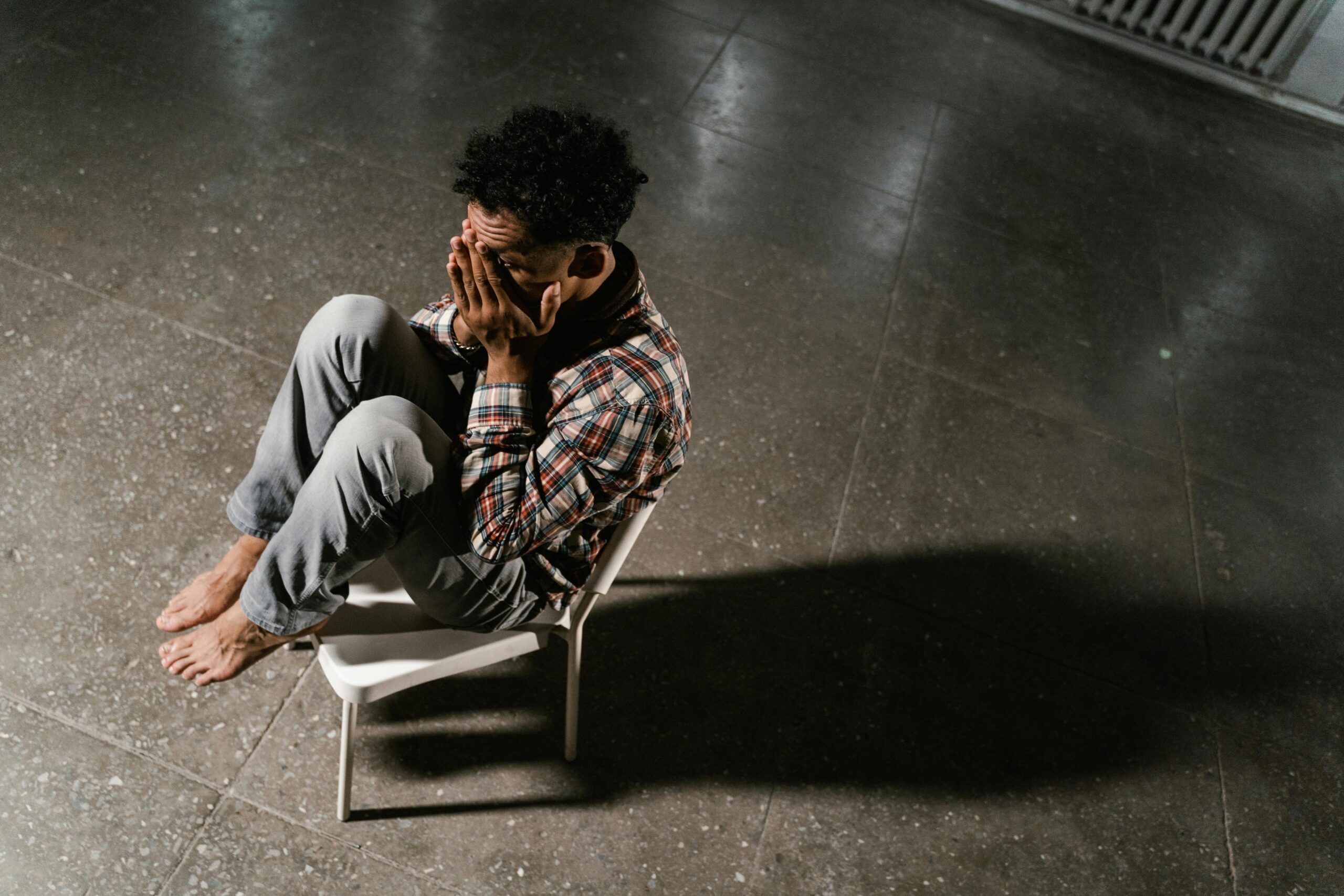 An overhead view of a man sitting alone in distress on a chair indoors, capturing anxiety and solitude.